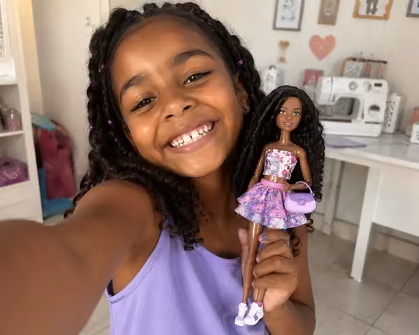 Menina sorrindo no ateli&ecirc; com fashion doll vestida com look artesanal