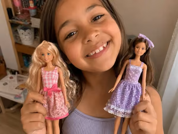 Menina segurando duas fashion dolls com vestidos artesanais